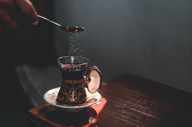 Foto close-up van een hand die suiker in een drankje op tafel giet