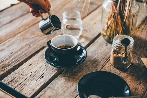Close-up van een hand die water in een koffiekop op tafel giet
