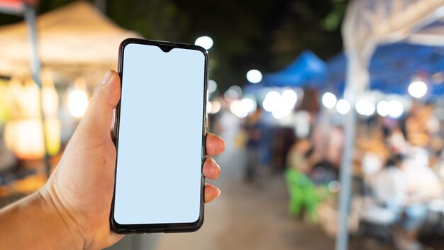 Close-up van een hand met een lege mobiele telefoon op een verlichte markt's nachts