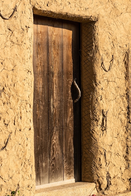 Close-up van een houten deur met bamboe deurklink en muurklei verlicht door zonlicht