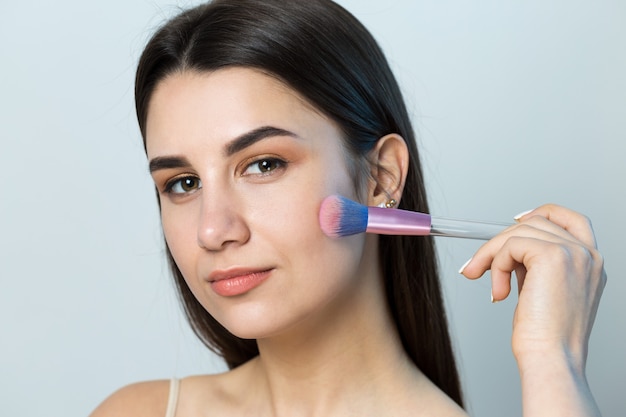 Close-up van een jong meisje in een lichte top op een witte achtergrond die een gezichtsmake-up maakt