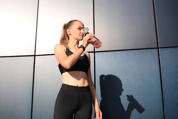 Close up van een jonge aantrekkelijke vermoeide sportvrouw buitenshuis, drinkwater uit een fles.