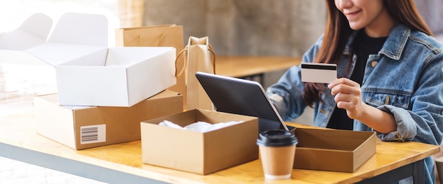 Close-up van een jonge Aziatische vrouw die tabletpc en creditcard voor het online winkelen met postpakketvakje en het winkelen zakken op de lijst gebruiken