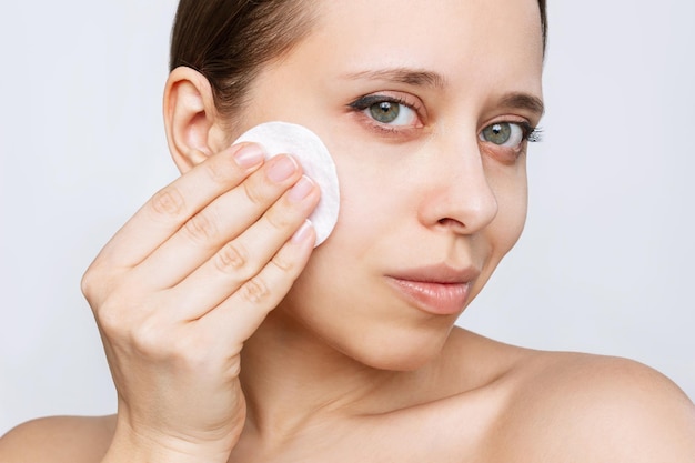 Close-up van een jonge blanke vrouw die haar gezicht schoonmaakt met lotion met een wattenschijfje