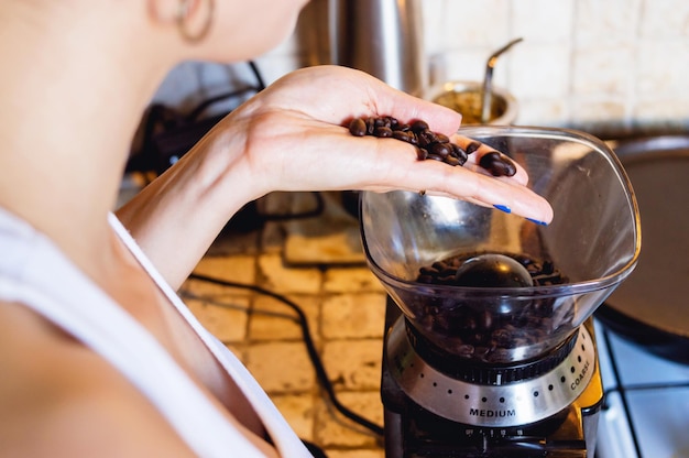 Close-up van een jonge blanke vrouw in de keuken die koffiebonen in een elektrische molen giet