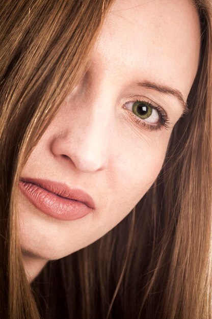 Foto close-up van een jonge blonde vrouw met lang haar dat haar rechteroog bedekt en naar de camera kijkt