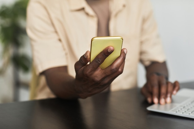 Close-up van een jonge man die aan tafel zit met een laptop en zijn mobiele telefoon aansluit op de computer