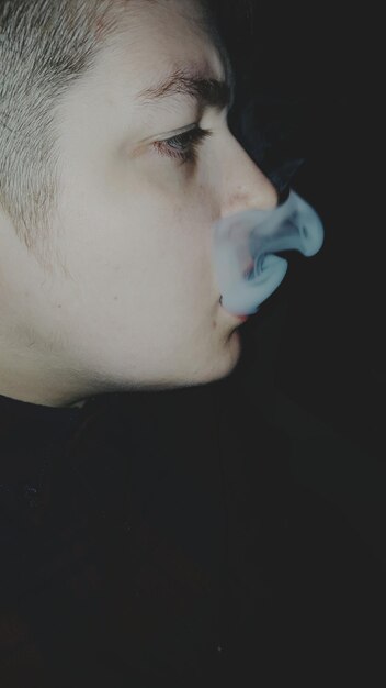 Close-up van een jonge man die op een zwarte achtergrond rookt