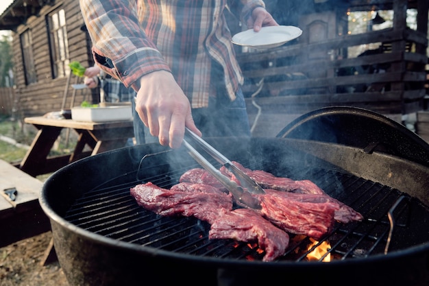 Close-up van een jonge man die plakjes vlees op de barbecue frituurt voor het diner buitenshuis