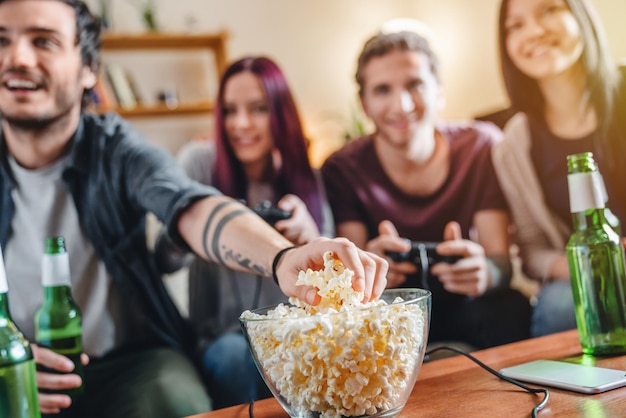 Close-up van een jonge man die popcorn neemt terwijl vrienden videogames spelen