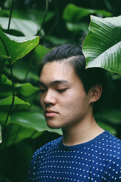 Foto close-up van een jonge man die wegkijkt terwijl hij bij planten in het park staat