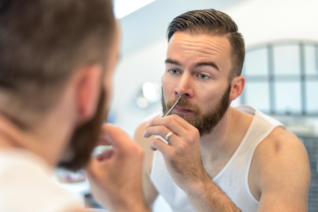 Foto close-up van een jonge man die zijn baard snijdt en zich thuis in de spiegel reflecteert