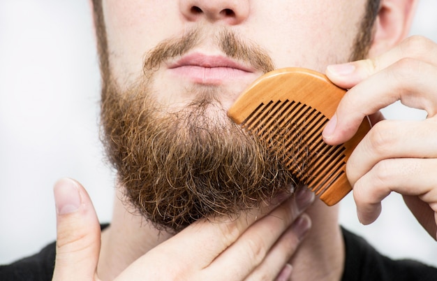 Close-up van een jonge man die zijn lange baard met een kam stileert terwijl hij alleen staat