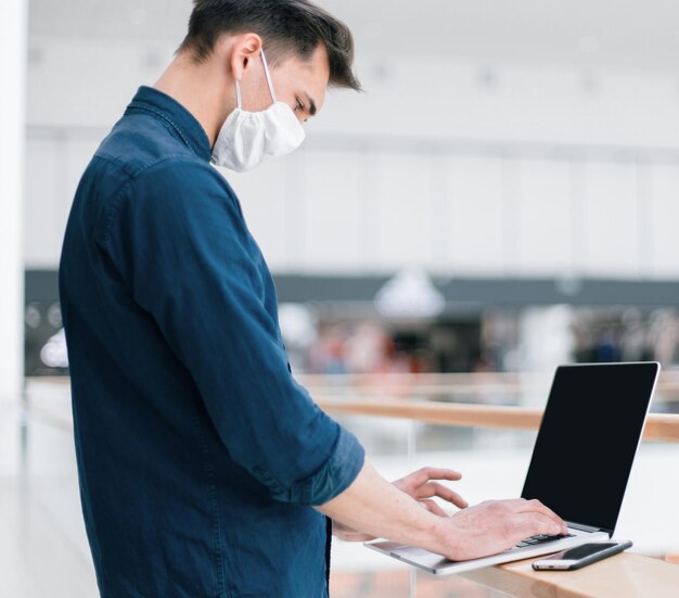 Close-up van een jonge man met een beschermend masker met behulp van een laptop