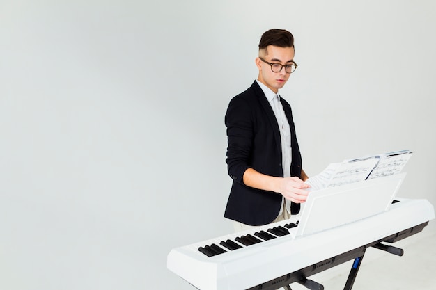 Close-up van een jonge mens die de pagina&#39;s van muzikaal blad op piano draait die op witte achtergrond wordt geïsoleerd