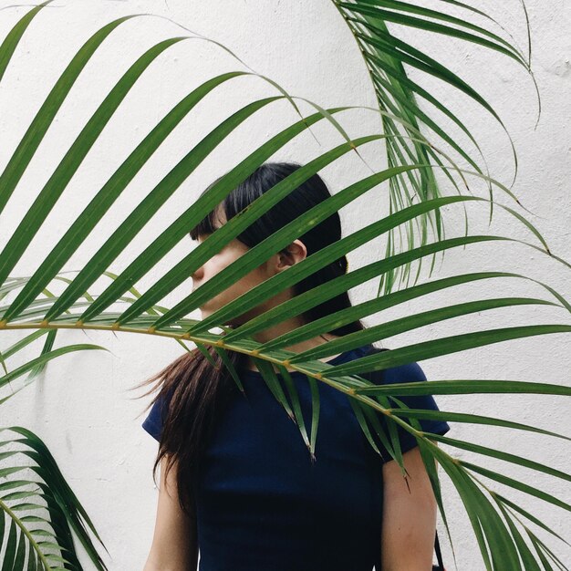 Foto close-up van een jonge vrouw achter palmbladeren tegen de muur