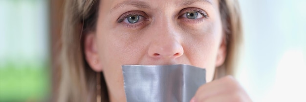 Close-up van een jonge vrouw die ducttape losmaakt op mondbeperking van de vrijheid van meningsuiting en