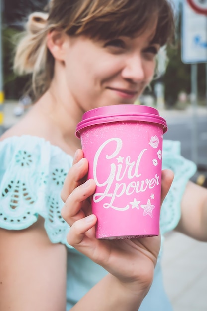 Foto close-up van een jonge vrouw die girl power tekst toont op een roze wegwerpbeker