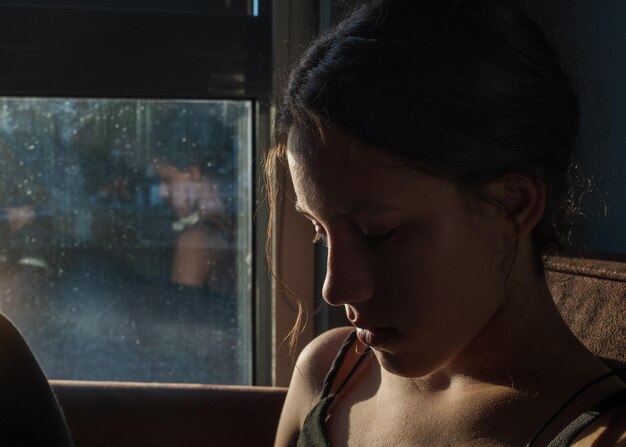 Close-up van een jonge vrouw die naar beneden kijkt bij het raam