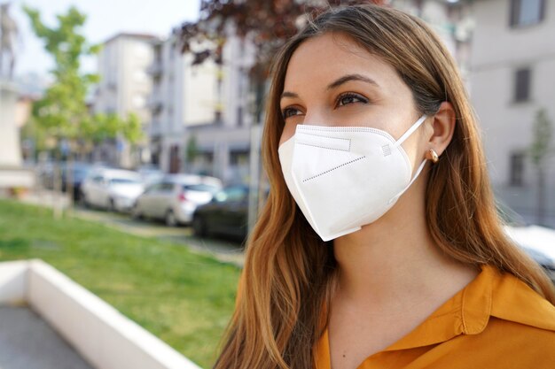 Close-up van een jonge vrouw die naar de zijkant kijkt terwijl ze buitenshuis een beschermend masker KN95 FFP2 draagt