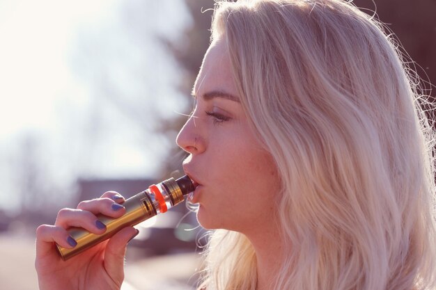 Foto close-up van een jonge vrouw met blond haar die een elektronische sigaret rookt