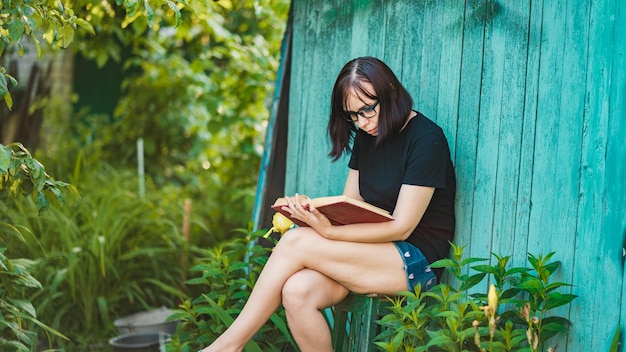 Close up van een jonge vrouw met een bril die een boek leest in de tuin Vrouw rust in de natuur en geniet van haar vrije tijd