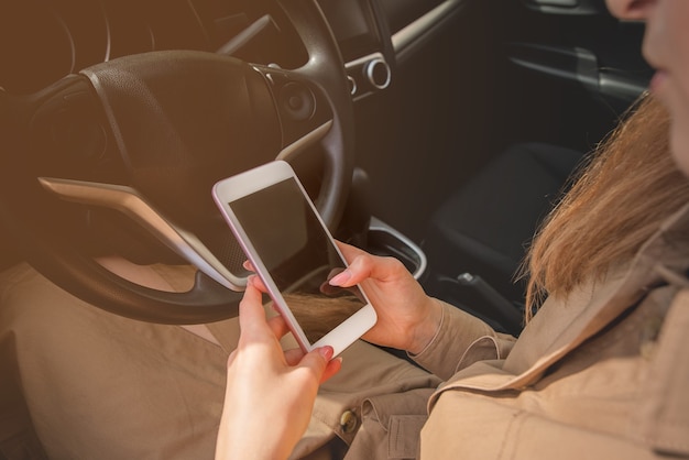 Close-up van een jonge zakenvrouw die haar smartphone bekijkt terwijl ze in de bestuurdersstoel van haar auto zit