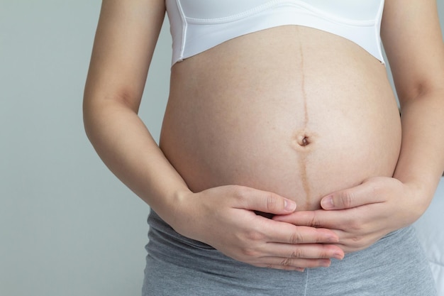 Close-up van een jonge zwangere vrouw die haar handen op haar buik houdt in het laatste trimester van de zwangerschap