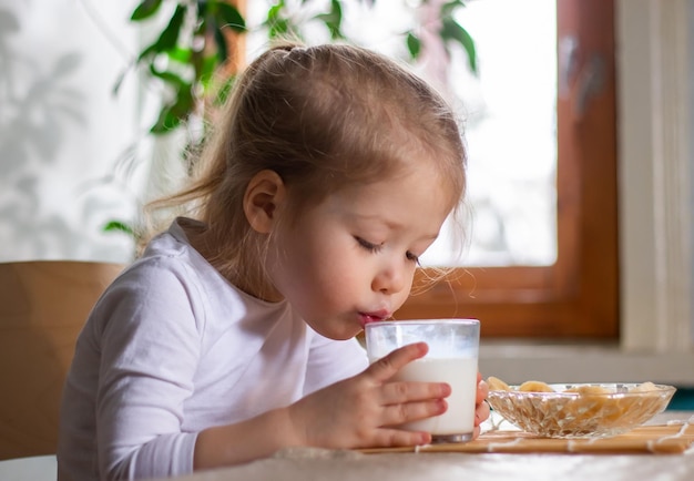 Close-up van een klein driejarig meisje dat een smakelijk ontbijt heeft en melk drinkt uit een glas