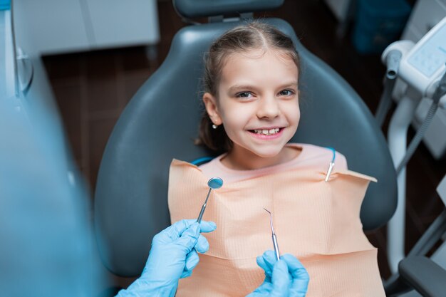 Close-up van een klein meisje dat in de tandartsstoel zit in de kliniek en zich voorbereidt op het onderzoek van haar tanden