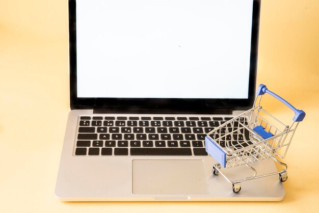 Close-up van een kleine winkelwagentje op een lege laptop tegen een gele achtergrond
