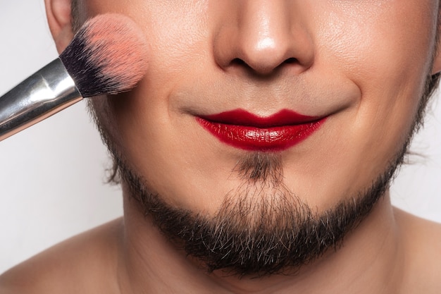 Close-up van een knappe bebaarde man die zijn eigen make-up doet.