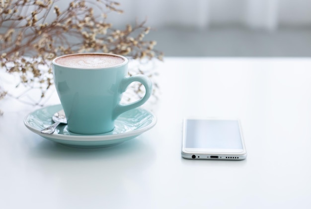 Close-up van een koffiekop met een smartphone op tafel