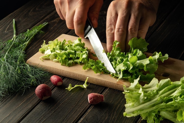 Close-up van een kok handen snijden groene bladeren sla op een snijplank met een mes