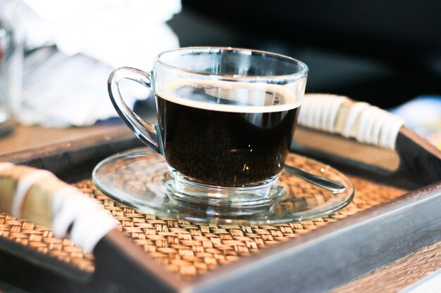 Foto close-up van een kop zwarte koffie geserveerd in een glazen beker op een dienblad