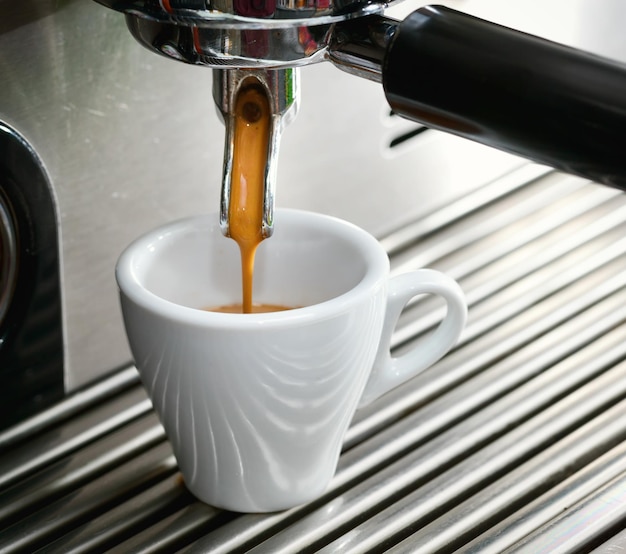 Foto close-up van een kopje en een koffieapparaat die espresso maken