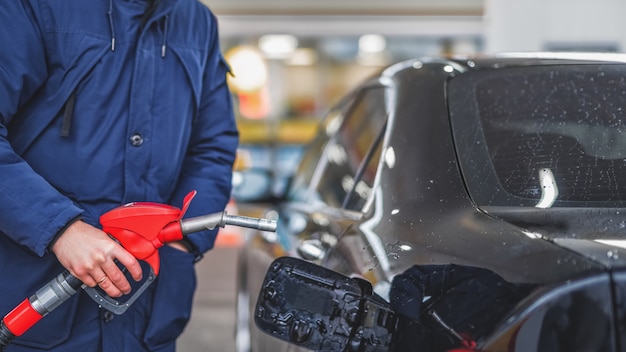 Close-up van een man die benzine in een auto pompt bij een benzinestation.