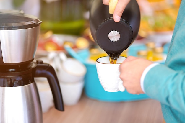 close-up van een man die koffie uit een koffiepot giet. zwarte koffiepot die koffie giet op een witte standaard.