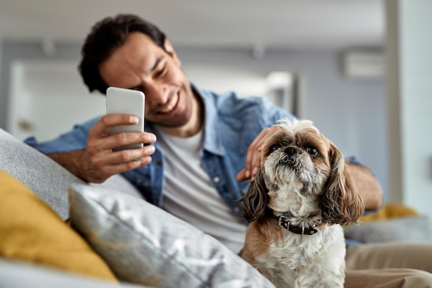 Close-up van een man die mobiele telefoon gebruikt terwijl hij ontspant met een hond in de woonkamer Focus ligt op hond