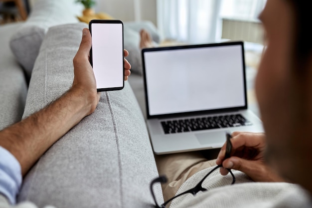 Close-up van een man die mobiele telefoon gebruikt terwijl hij ontspant op de bank en op laptop werkt