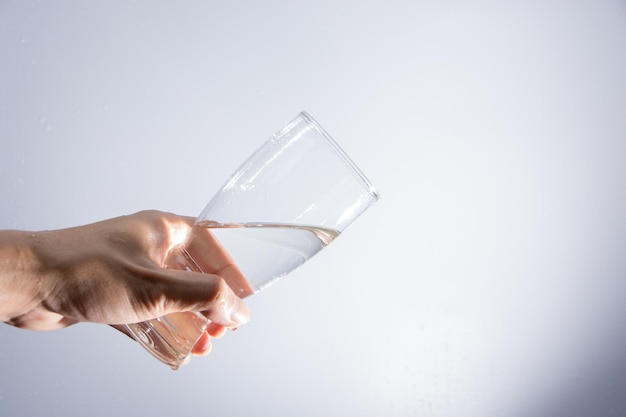 Foto close-up van een man die water uit een drinkglas giet tegen een grijze achtergrond