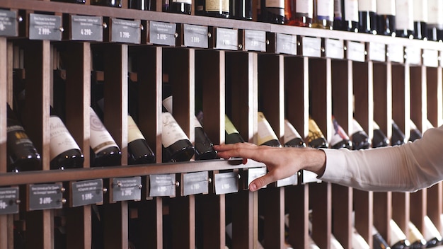 Close-up van een man hand die een fles wijn van een plank in een opslag selecteert