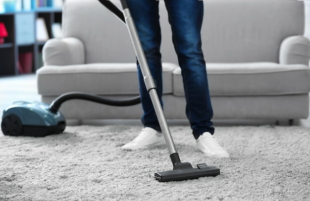 Close-up van een man met een stofzuiger die een tapijt thuis schoonmaakt