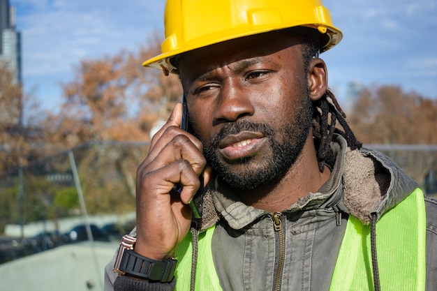 Close-up van een man van Afrikaanse afkomst, teleurgesteld werknemer van een bouwbedrijf die aan de telefoon praat.