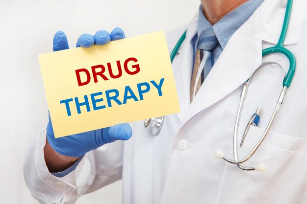 Close-up van een mannelijke arts die in handschoenen een bordje met de tekst Drugstherapie houdt