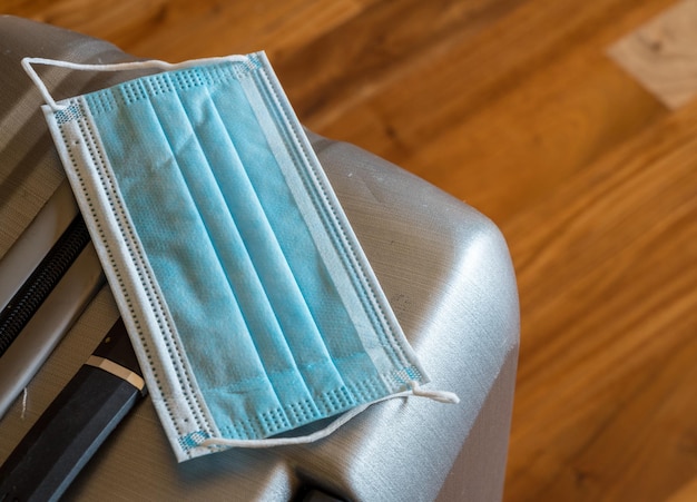 Close-up van een medisch gezichtsmasker op een koffer die klaar is om te reizen voor zaken of vakantie tijdens de coronavirusepidemie