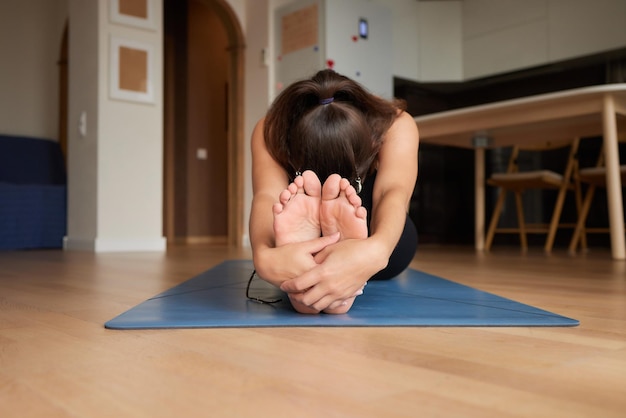 Close-up van een meisje dat zich uitstrekt om haar tenen aan te raken terwijl ze op een yogamat zit