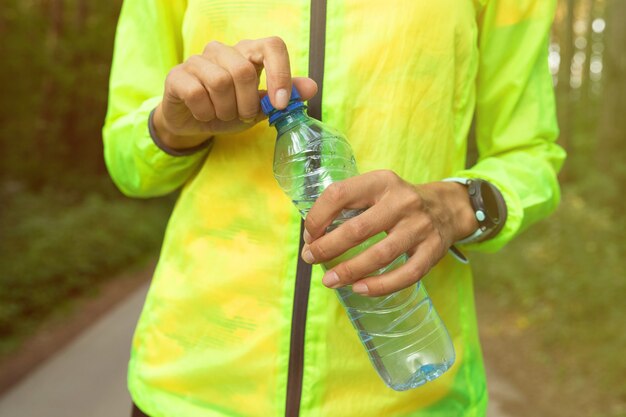 Foto close-up van een meisje dient een heldergroen windjack in dat een waterfles vasthoudt