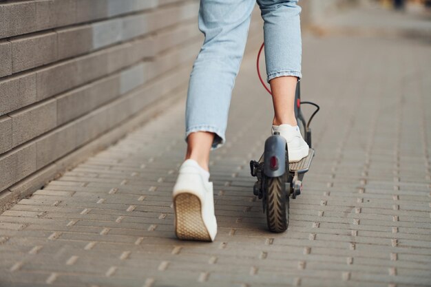 Close-up van een meisje in vrijetijdskleding die op een zonnige dag buiten op een elektrische schooter rijdt