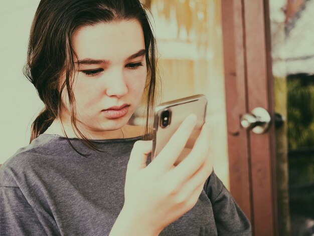 Foto close-up van een meisje met een mobiele telefoon terwijl ze thuis tegen de muur op een stoel zit